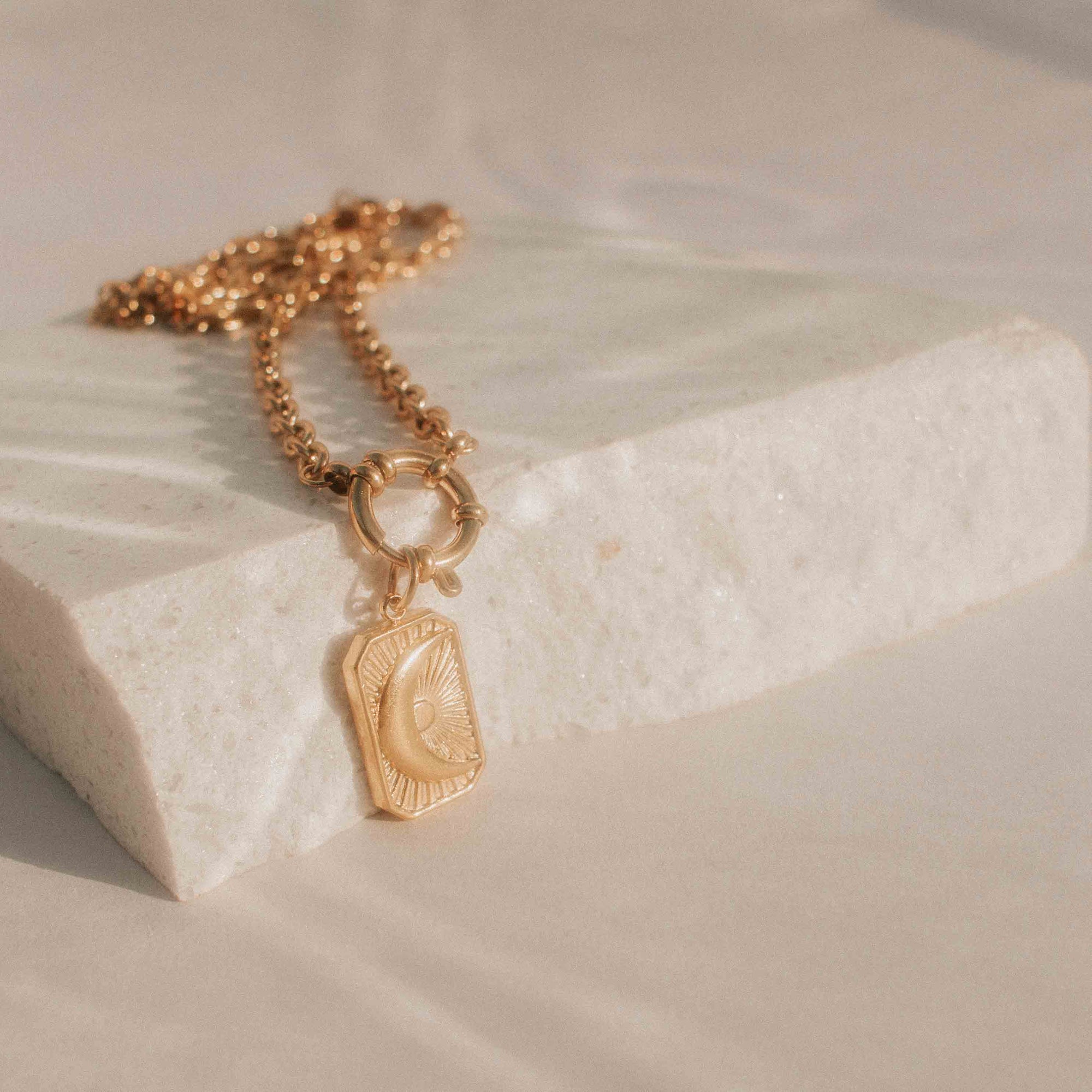Gold necklace with a pendant on a light stone surface